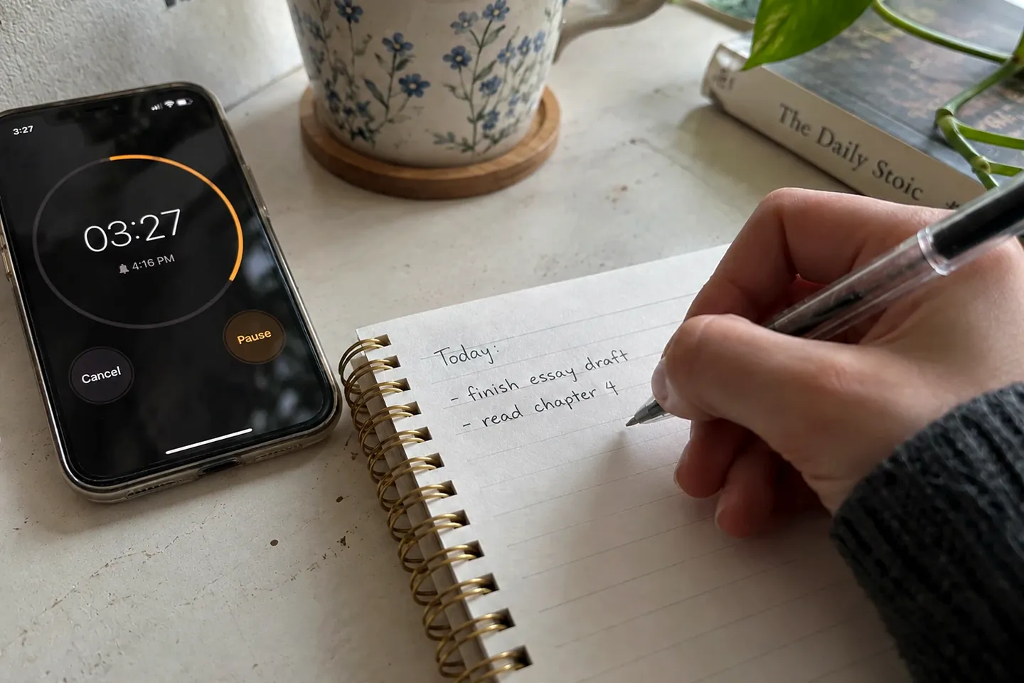 A hand writing a short list in a spiral notebook, next to a phone showing a timer with a few minutes left.